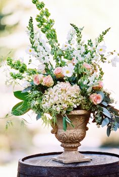 a vase filled with lots of flowers sitting on top of a wooden barrel covered in greenery