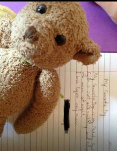 a brown teddy bear sitting on top of a piece of paper next to a pen