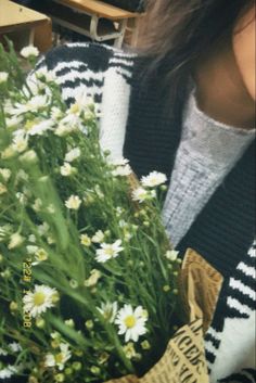 a woman holding a bouquet of daisies in her hands