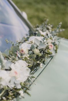 flowers and greenery are arranged on the hood of an old car, with grass in the background