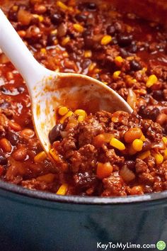 a spoon full of chili and corn in a pot