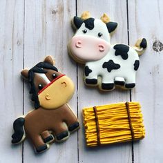 two decorated cookies sitting next to each other on a white wooden surface, one has a cow and the other is a horse