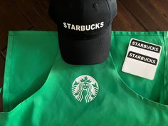 the starbucks hat is sitting on top of a green apron and black starbuck's baseball cap