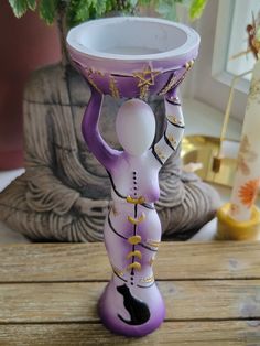 a purple and white vase sitting on top of a wooden table next to a potted plant