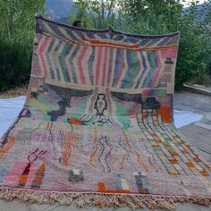 a multicolored area rug on the ground with trees in the backgroud