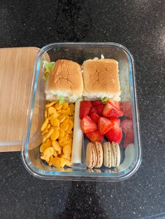 a plastic container filled with sandwiches, fruit and crackers next to a cutting board