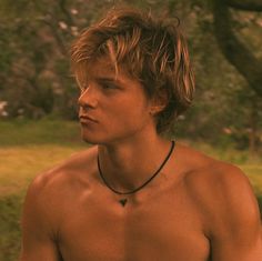 a shirtless young man holding a frisbee in front of his face and looking off into the distance