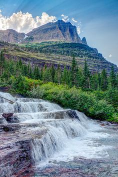 a waterfall with trees and mountains in the background