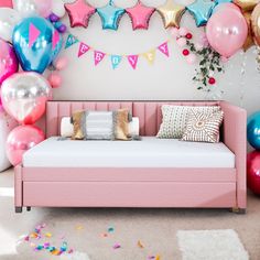 a pink daybed in front of balloons and confetti on the wall behind it