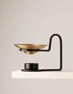 a brass bowl on a black stand with a white wall in the backgroud