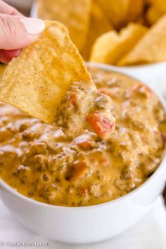 a hand holding a tortilla chip and dipping it into a white bowl filled with salsa