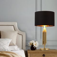 a lamp that is on top of a night stand next to a bed with pillows