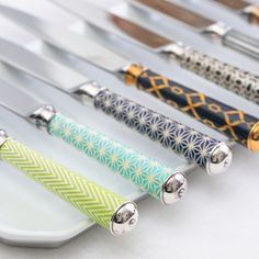 several knives are lined up on a white plate with silver handles and knobs in different patterns