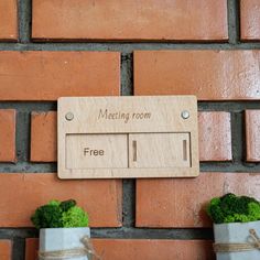 a wooden sign that says meeting room free on the side of a brick wall next to two small potted plants