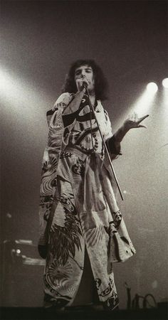 a man standing on top of a stage with a microphone in his hand and lights behind him