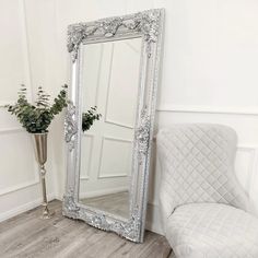 a large silver mirror sitting on top of a wooden floor next to a white chair