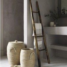 two baskets sitting next to each other in front of a bathtub with a ladder leaning up against the wall