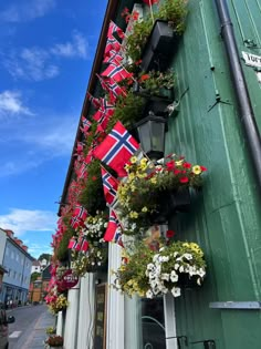 flags and flowers are hanging from the side of a building on a street in norway