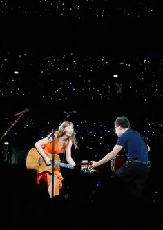 a man and woman playing guitar in front of a stage with stars on the ceiling