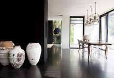 three large vases sitting on top of a black floor next to a dining room table