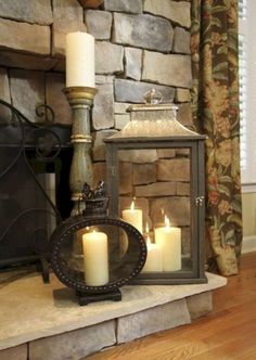 candles are lit in front of a fireplace with a stone wall behind it and an iron lantern on the mantle