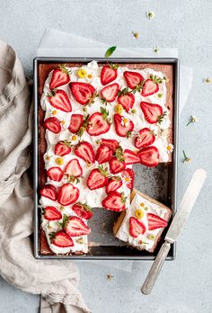 a square cake with strawberries on top is sitting on a table next to a knife and fork