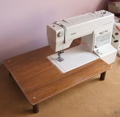 a white sewing machine sitting on top of a wooden table next to a pink wall