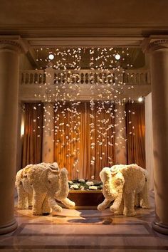 two elephants standing in the middle of a room with columns and chandeliers hanging from the ceiling