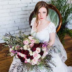 a woman in a white dress holding a bouquet of flowers on her wedding day with a brick wall behind her