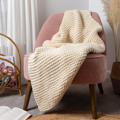 a pink chair with a blanket on top of it next to a book and potted plant