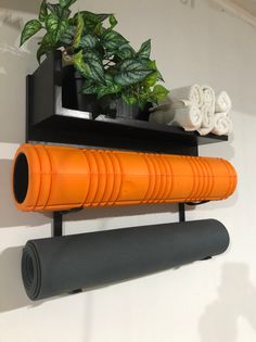 an orange yoga mat is on the wall next to a black shelf with towels and a potted plant