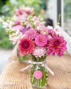 pink and white flowers sit in vases on a wooden table with ribbon tied around them