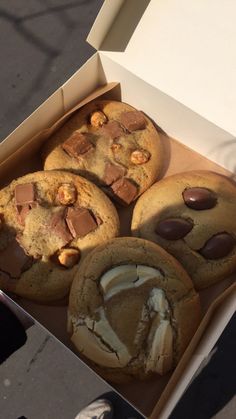 an open box of cookies with chocolate chips and marshmallows on top, sitting on the ground