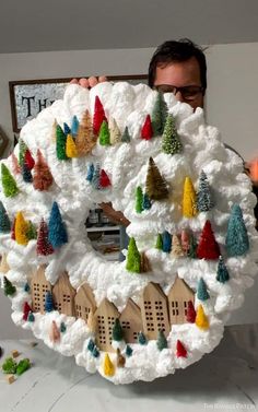 a man holding up a large snow covered christmas tree with houses and trees on it