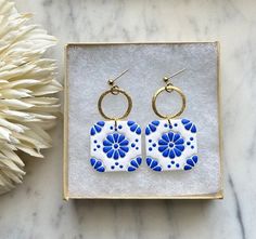 a pair of blue and white earrings sitting on top of a marble table next to a flower