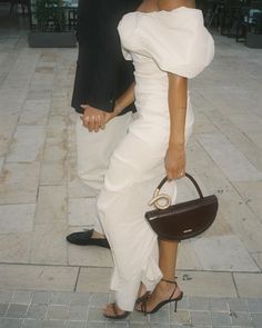 a man and woman standing next to each other on a sidewalk with one holding a purse