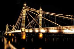 a bridge that is lit up at night with lights all around it and reflecting in the water