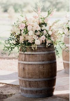 a wooden barrel with flowers and greenery in it sitting on the ground next to two wine barrels