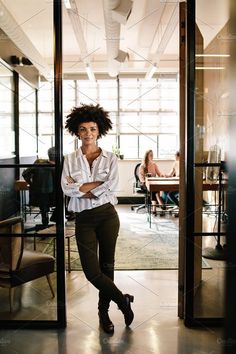 a woman standing in an office doorway with her arms crossed and looking at the camera