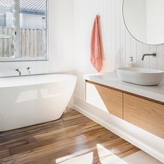 a white bath tub sitting next to a sink under a bathroom mirror on top of a wooden counter