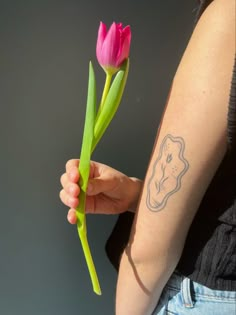 a woman holding a pink flower in her right arm with a tattoo on it's left arm