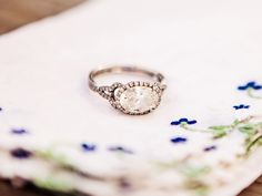 a diamond ring sitting on top of a white surface next to blue and purple flowers