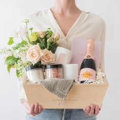 a woman holding a wooden box filled with lots of different types of cosmetics and flowers