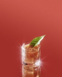 a tall glass filled with ice and a green leaf on top, sitting on a red surface