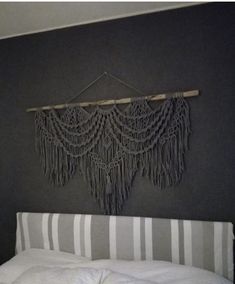 a white bed sitting next to a gray wall with fringes hanging from it's headboard