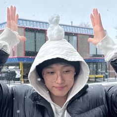 a young man wearing glasses and a hooded jacket is holding his hands up in the air