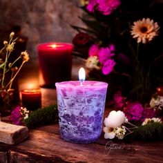 a purple candle sitting on top of a wooden table next to some flowers and candles