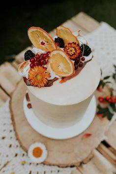 a white cake with fruit and flowers on top is sitting on a wooden table outdoors