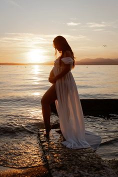 a pregnant woman standing in the water at sunset