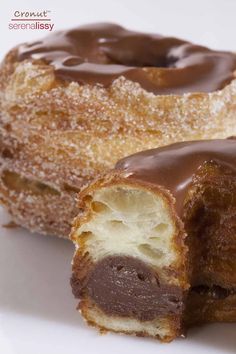 two chocolate covered doughnuts sitting on top of a white plate next to each other